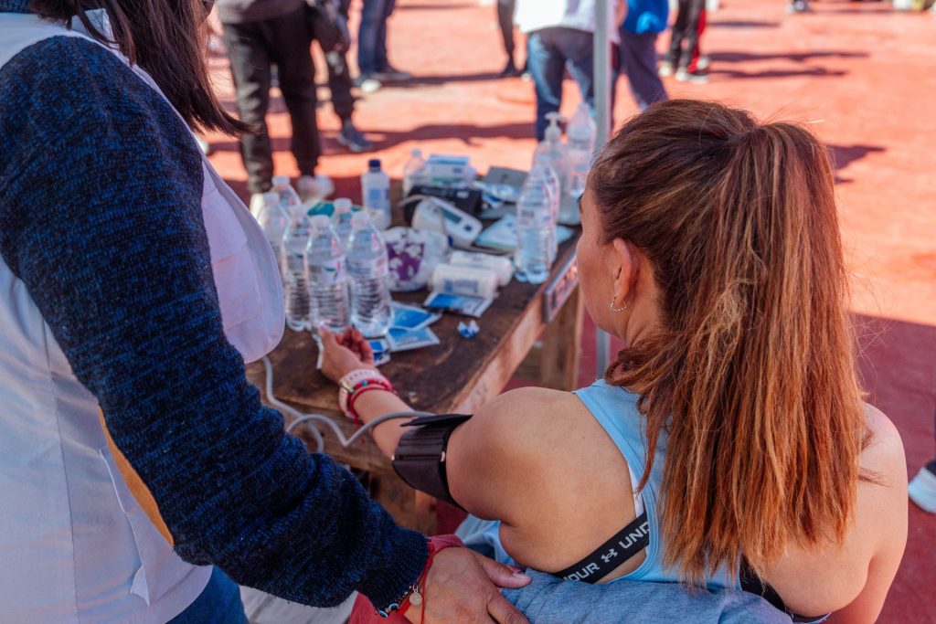 Mujer con ropa deportiva sometiéndose a un control de salud al aire libre durante un evento deportivo.